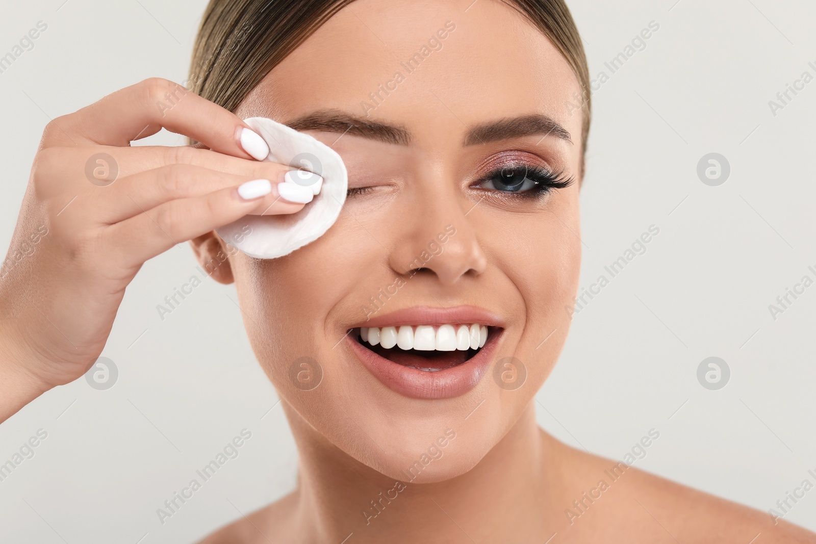 Photo of Beautiful woman removing makeup with cotton pad on light grey background, closeup