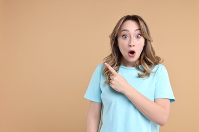 Portrait of surprised woman pointing at something on beige background. Space for text