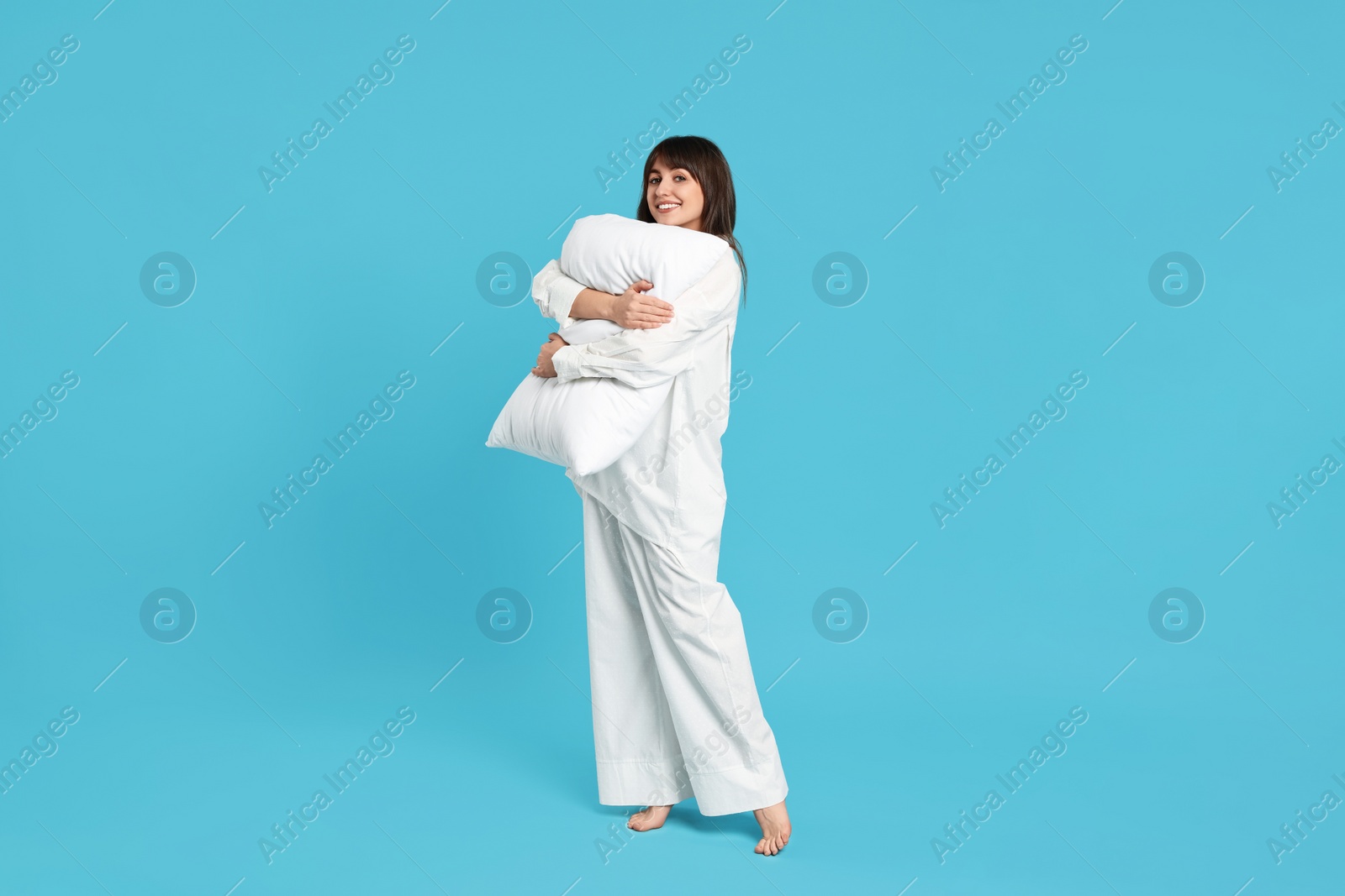 Photo of Happy woman in pyjama holding pillow on light blue background