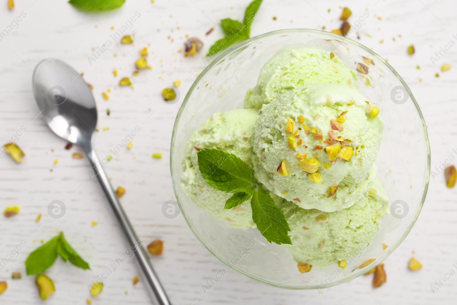 Photo of Delicious green ice cream served in dessert bowl on white wooden table, top view