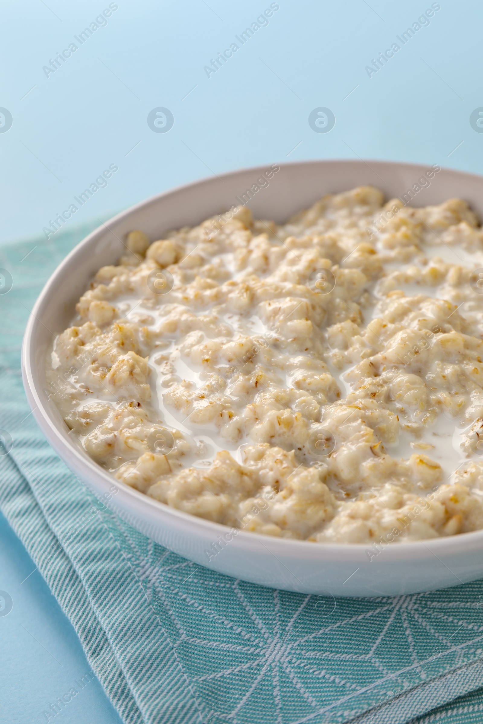 Photo of Tasty boiled oatmeal in bowl on light blue table, closeup