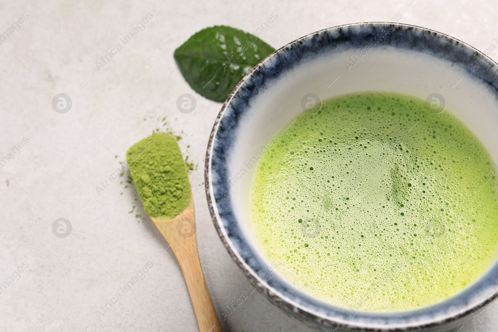 Photo of Cup of matcha tea and bamboo spoon with green powder on light gray table, above view. Space for text