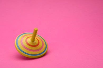 Photo of One bright spinning top on pink background, space for text. Toy whirligig