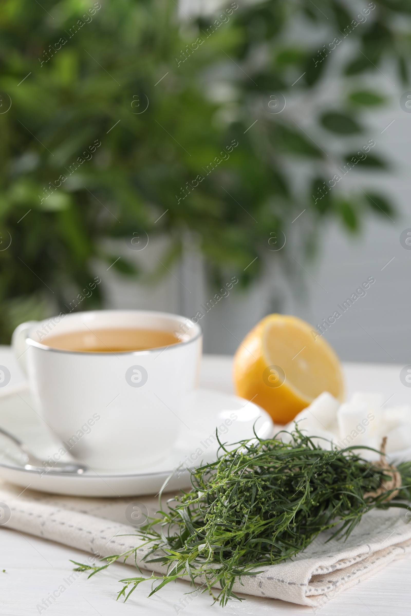 Photo of Aromatic herbal tea, fresh tarragon sprigs, sugar cubes and lemon on white table, space for text