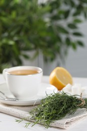 Aromatic herbal tea, fresh tarragon sprigs, sugar cubes and lemon on white table, space for text