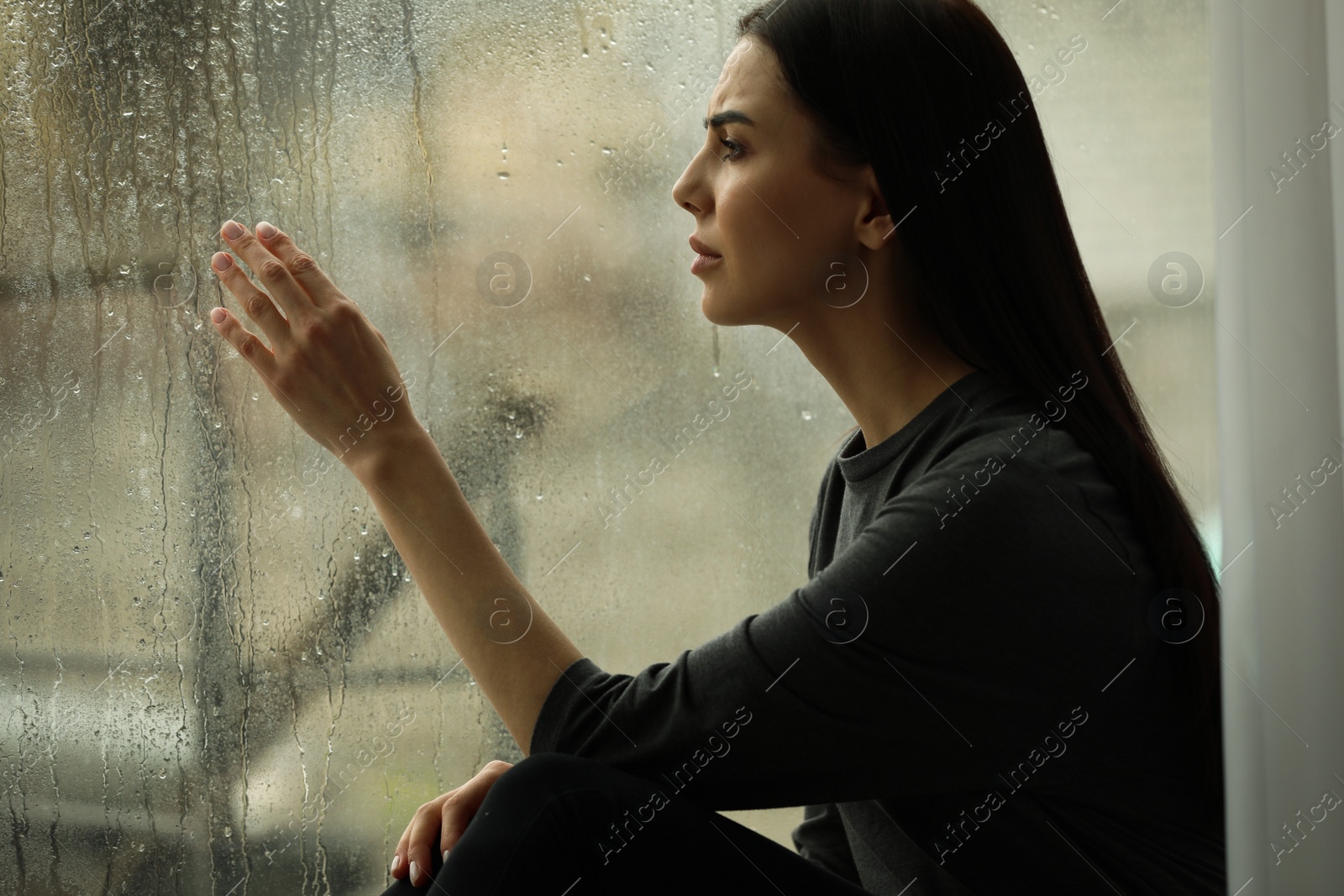 Photo of Depressed woman near window on rainy day