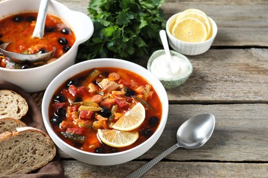 Photo of Meat solyanka soup with sausages, olives and vegetables served on wooden table