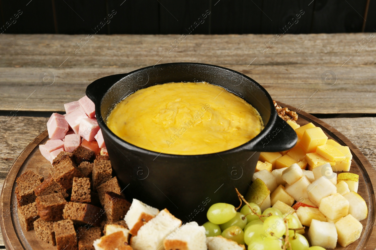 Photo of Fondue pot with melted cheese and different products on wooden table, closeup