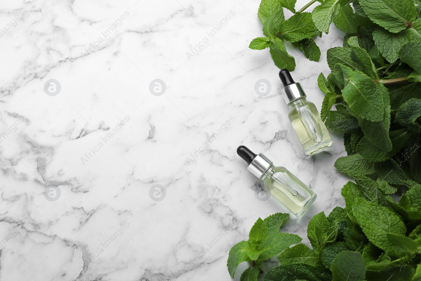 Photo of Bottles of mint essential oil and green leaves on white marble table, flat lay. Space for text