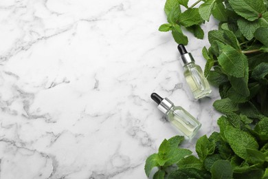 Photo of Bottles of mint essential oil and green leaves on white marble table, flat lay. Space for text