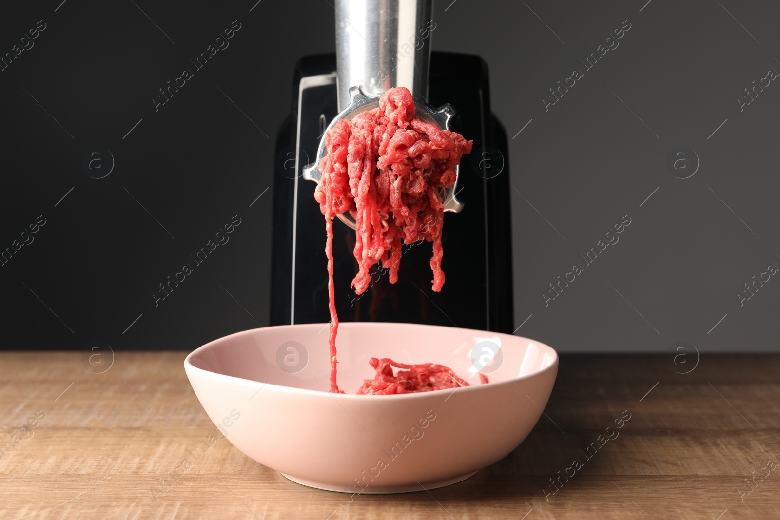 Photo of Electric meat grinder with beef mince on wooden table against grey background
