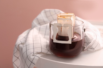 Photo of Glass cup with drip coffee bag on small white table, closeup
