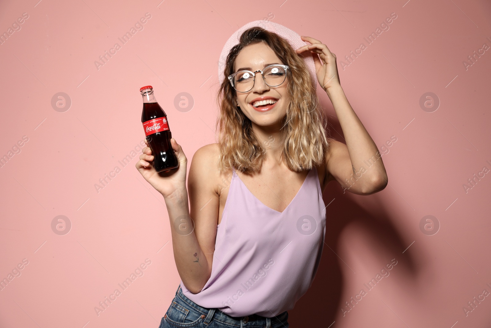 Photo of MYKOLAIV, UKRAINE - NOVEMBER 28, 2018: Young woman with bottle of Coca-Cola on color background