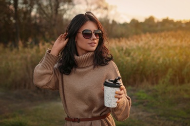 Photo of Beautiful young woman with cupcoffee wearing stylish autumn sweater outdoors