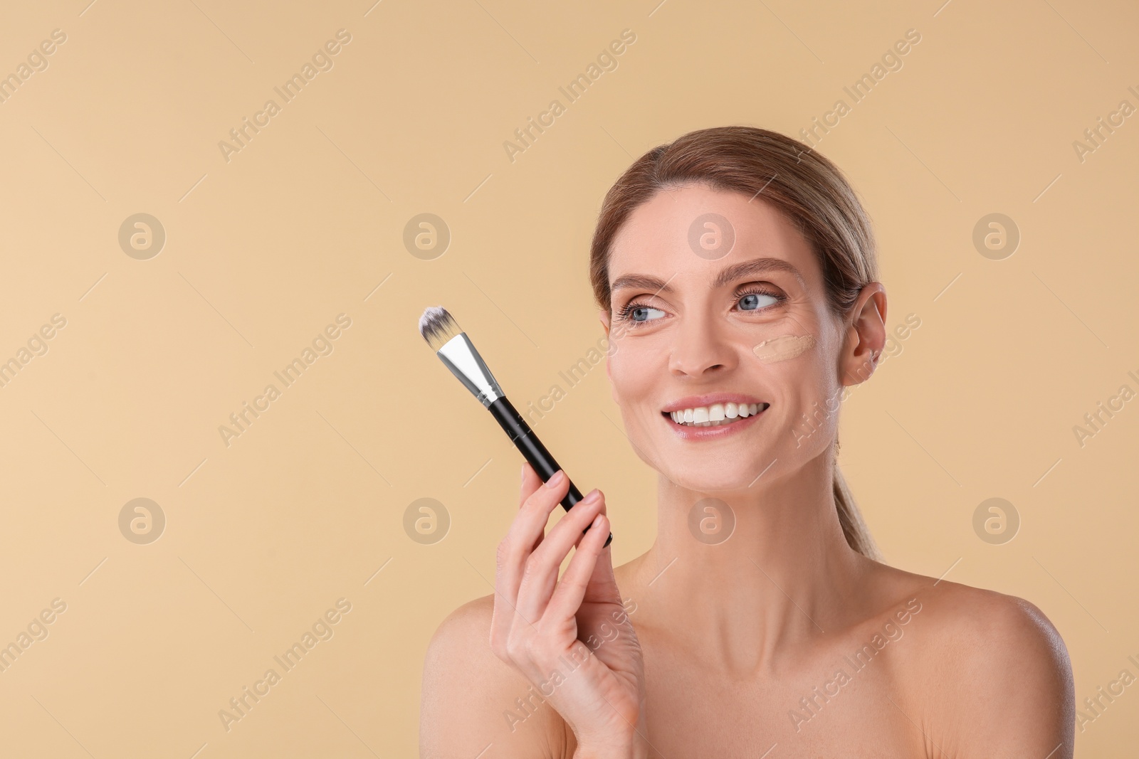 Photo of Woman with swatch of foundation holding makeup brush on beige background. Space for text