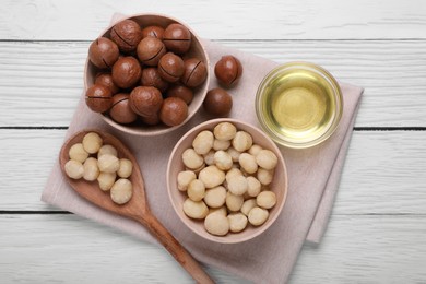 Delicious organic Macadamia nuts and natural oil on white wooden table, top view