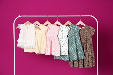 Rack with stylish child clothes on color background