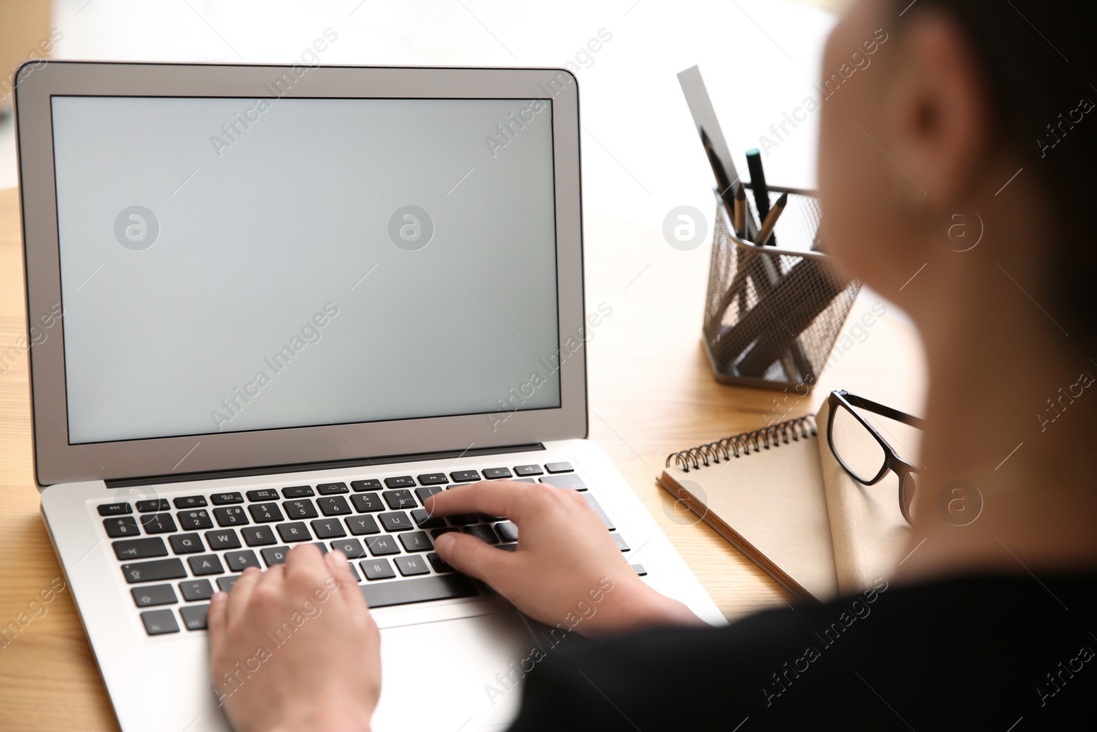 Photo of Woman working with modern laptop at wooden table, closeup. Space for design