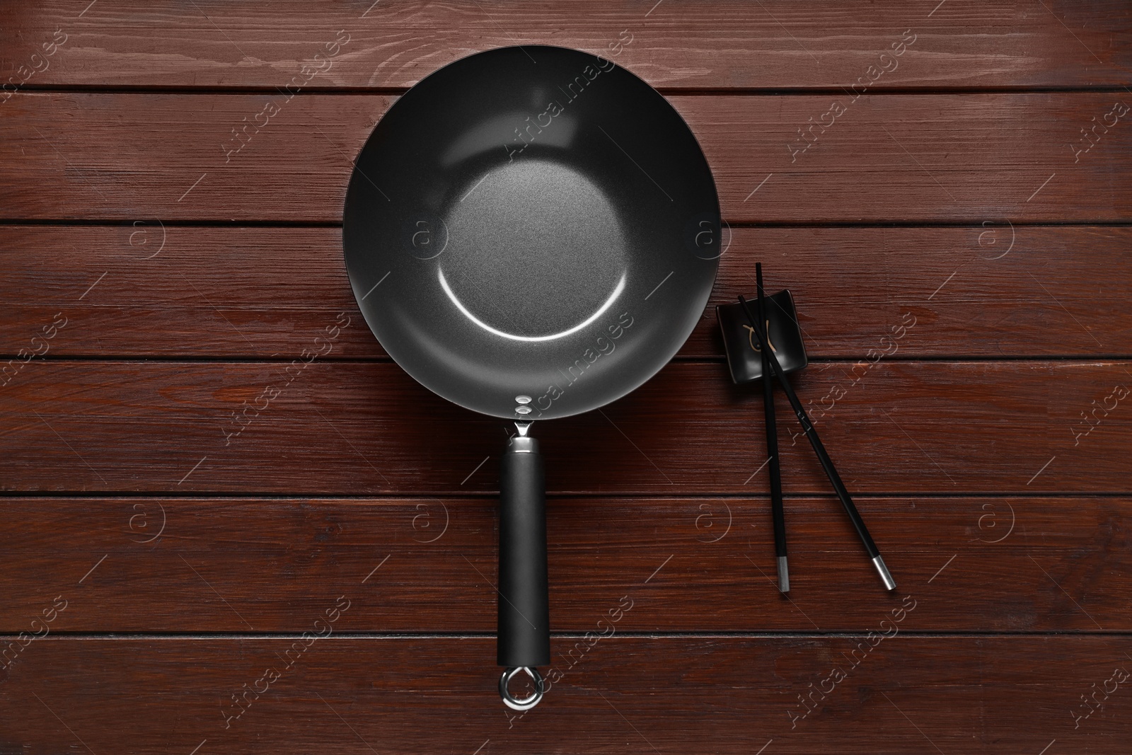 Photo of Empty iron wok and chopsticks on wooden table, flat lay