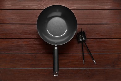 Empty iron wok and chopsticks on wooden table, flat lay