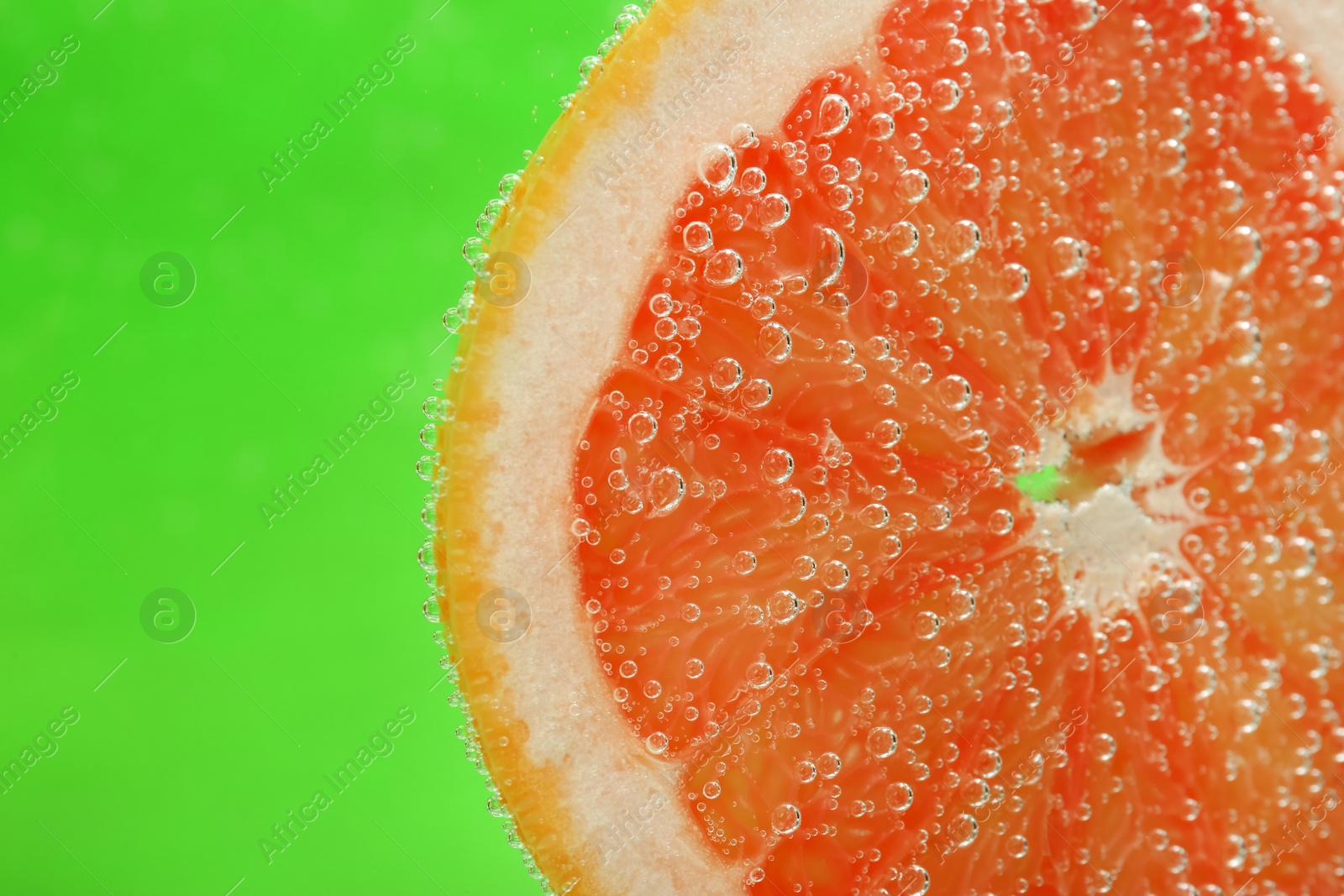 Photo of Slice of grapefruit in sparkling water on green background, closeup with space for text. Citrus soda