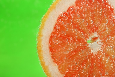 Photo of Slice of grapefruit in sparkling water on green background, closeup with space for text. Citrus soda