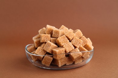 Photo of Brown sugar cubes in bowl on color background, closeup