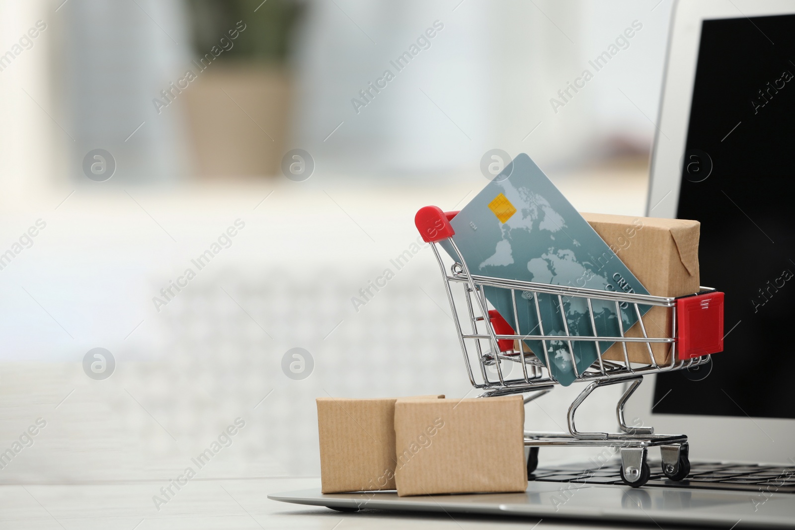 Photo of Online payment concept. Small shopping cart with bank card, boxes and laptop on table, space for text