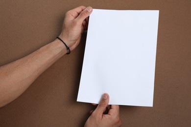 Photo of Man holding sheet of paper on brown background, closeup. Mockup for design