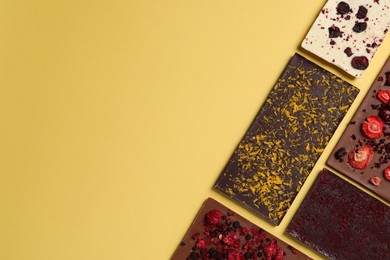 Photo of Different chocolate bars with freeze dried fruits on yellow background, flat lay. Space for text