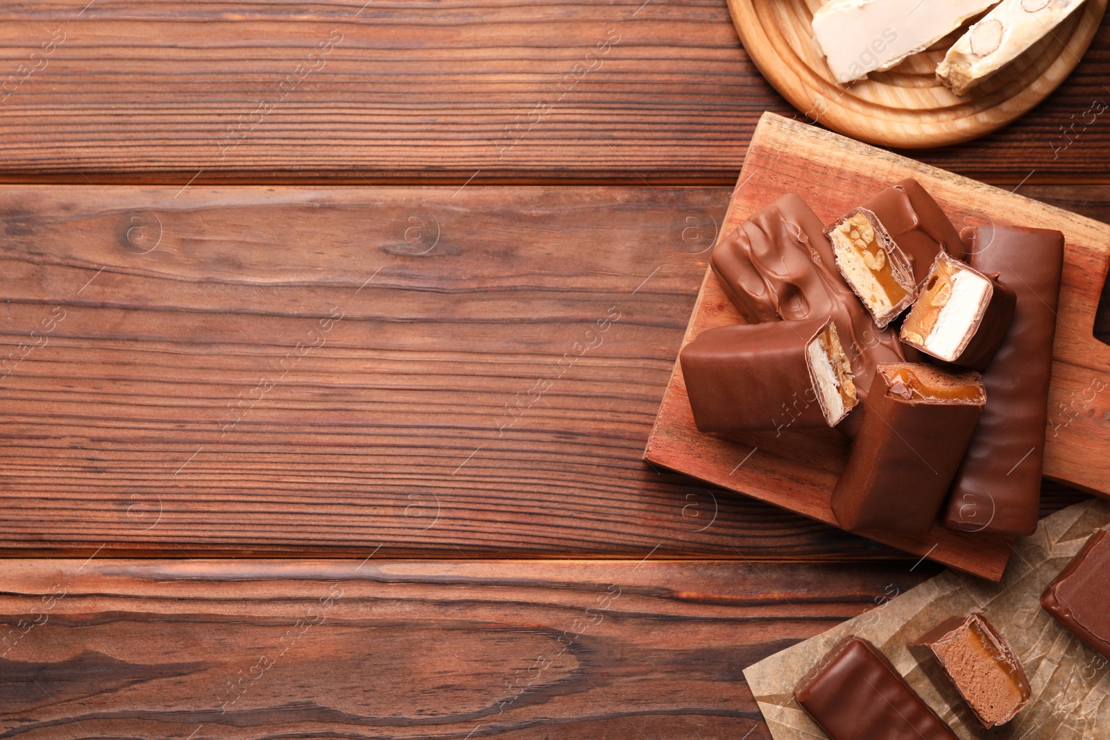 Photo of Tasty chocolate bars with nougat, caramel and nuts on wooden table, flat lay. Space for text