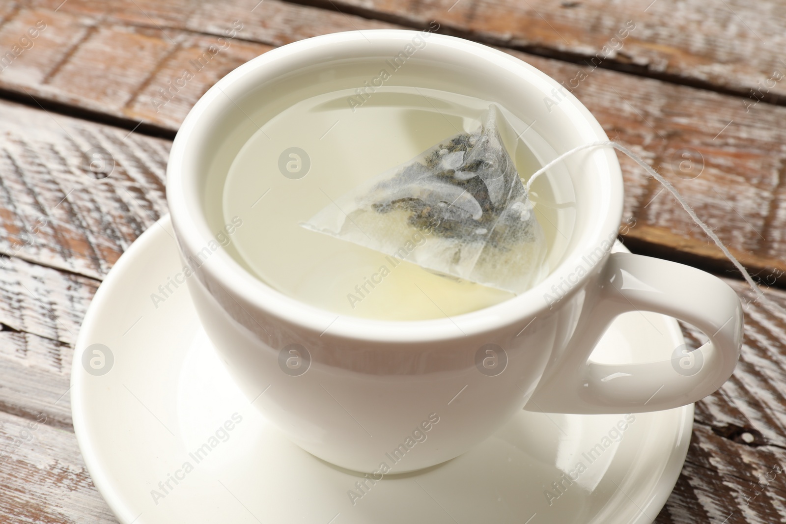 Photo of Tea bag in cup with hot water on wooden rustic table, closeup