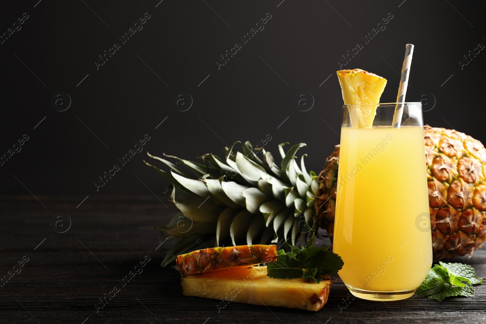 Photo of Delicious pineapple juice and fresh fruit on black wooden table. Space for text