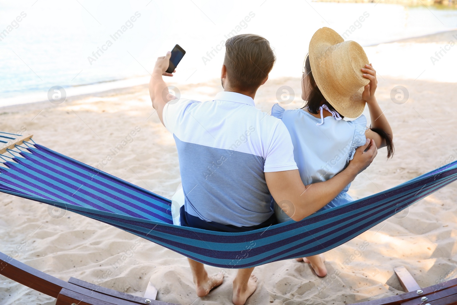 Photo of Young couple taking selfie in hammock at seaside