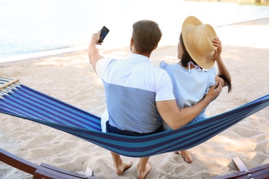 Photo of Young couple taking selfie in hammock at seaside