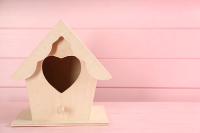 Beautiful bird house on pink wooden table, space for text