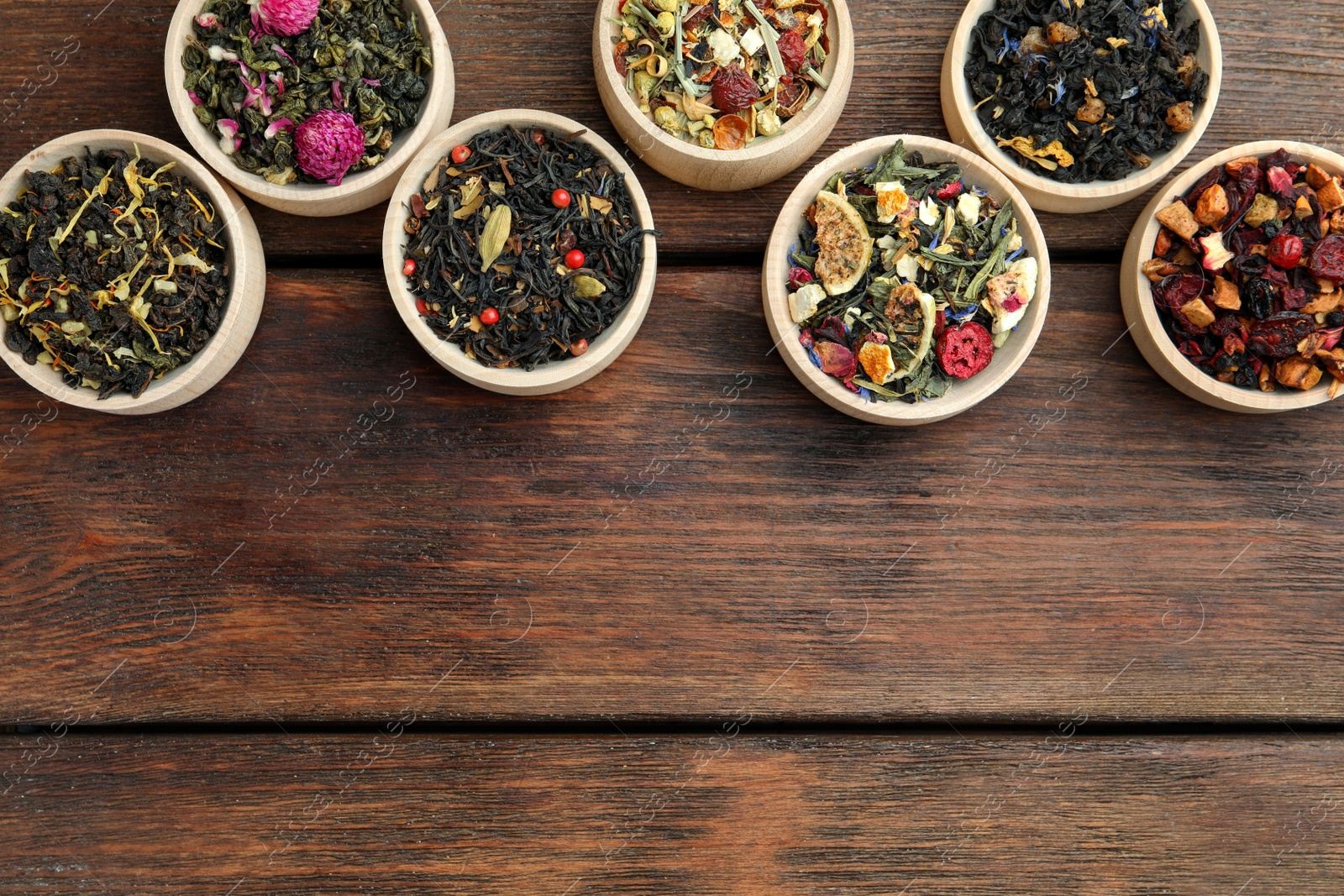 Photo of Different kinds of dry herbal tea in bowls on wooden table, flat lay. Space for text