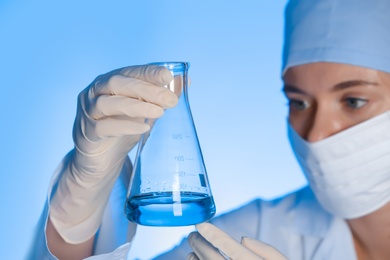 Female scientist holding test flask with sample on color background. Chemical analysis