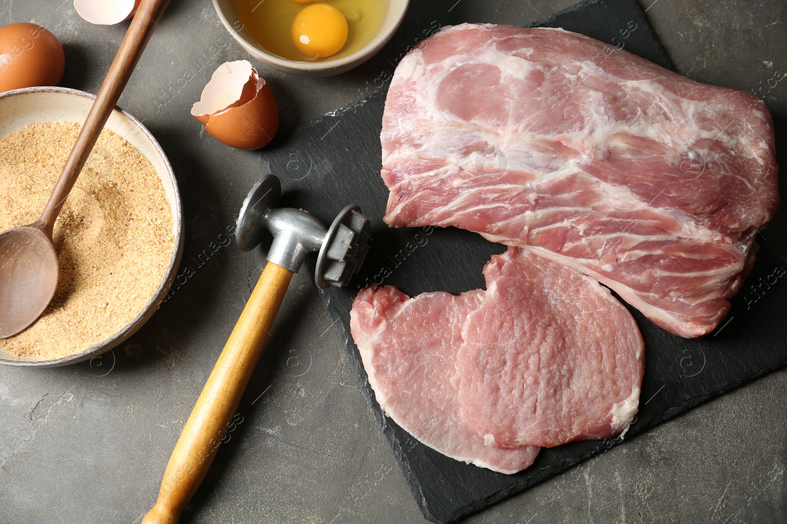 Photo of Raw pork chops and ingredients for cooking schnitzel on grey table, flat lay