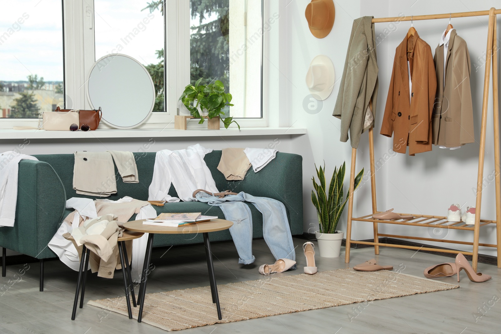 Photo of Messy pile of clothes on sofa and shoes in living room