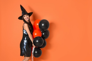 Beautiful woman wearing witch costume with balloons for Halloween party on yellow background, space for text