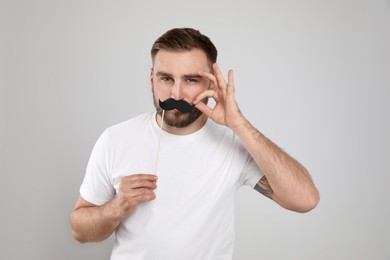 Photo of Funny man with fake mustache on light grey background