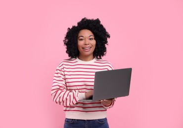 Happy young woman with laptop on pink background