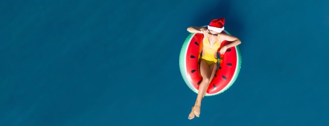 Image of Young woman wearing Santa hat and swimsuit with inflatable ring in sea, top view. Christmas vacation