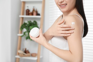 Young woman applying body cream on shoulder in room, closeup. Space for text