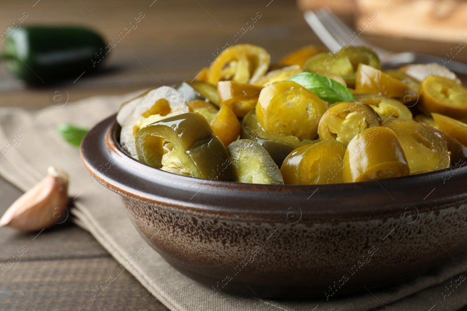 Photo of Bowl with slices of pickled green jalapeno peppers on wooden table, closeup