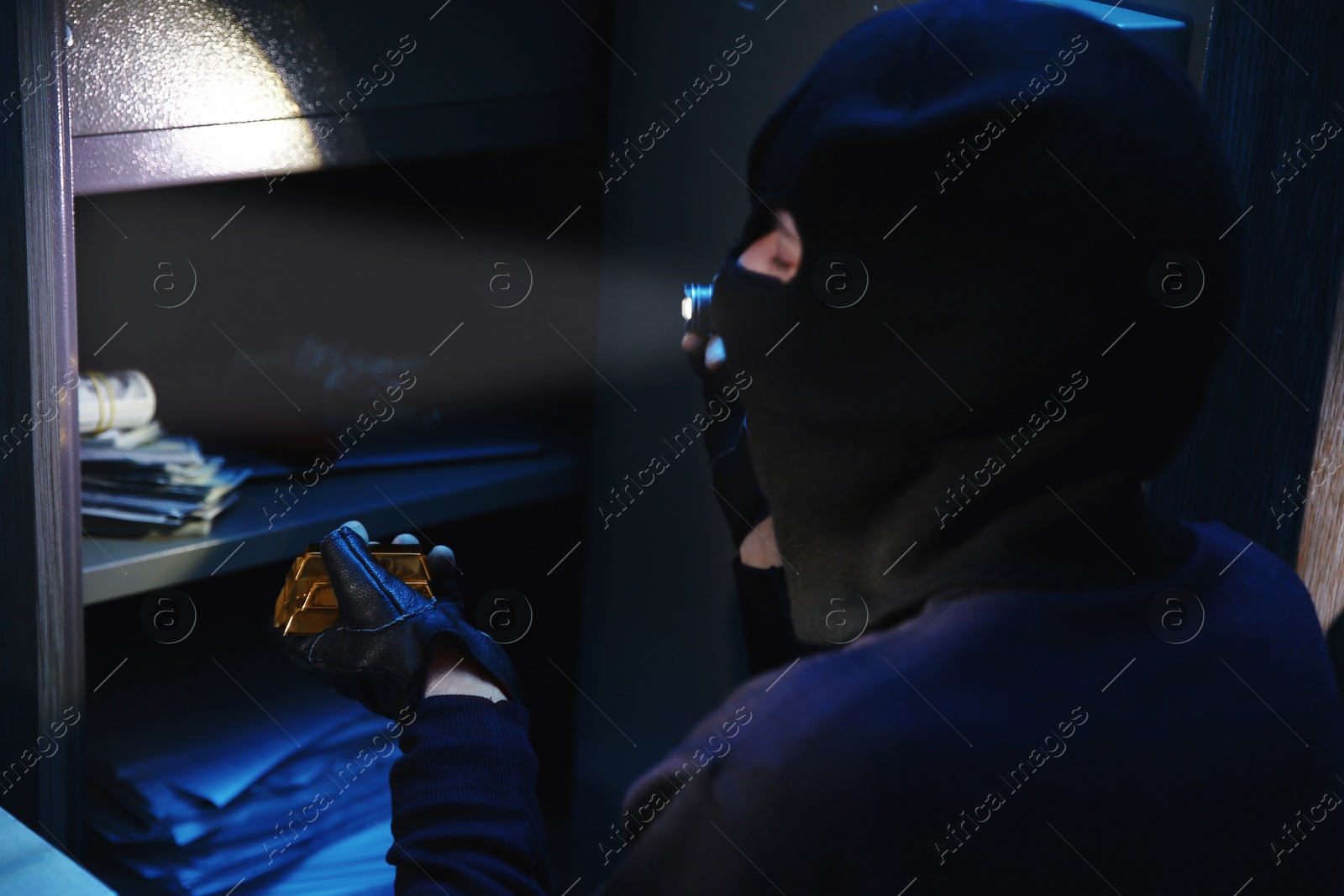 Photo of Thief taking gold bars out of steel safe indoors at night