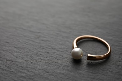 Photo of Elegant golden ring with pearl on black table. Space for text
