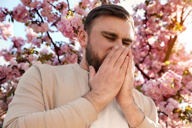 Man suffering from seasonal pollen allergy near blossoming tree outdoors