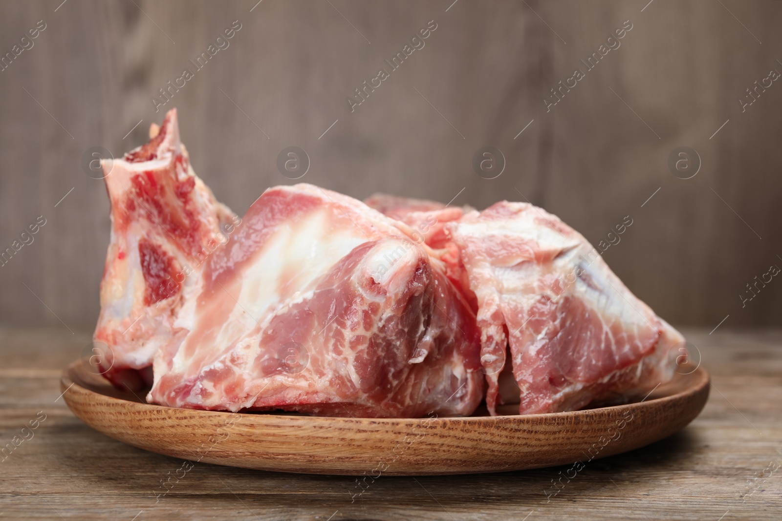 Photo of Plate with raw chopped meaty bones on wooden table